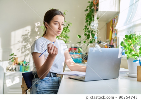 Teenage girl studying at home at the table using a laptop Teenage girl studying at home at the table using a laptop 90254743