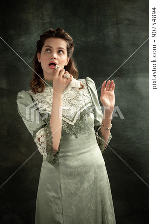 Vintage portrait of young beautiful girl in gray dress of medieval style isolated on dark background. Comparison of eras concept, flemish style. Art, beauty 90254894