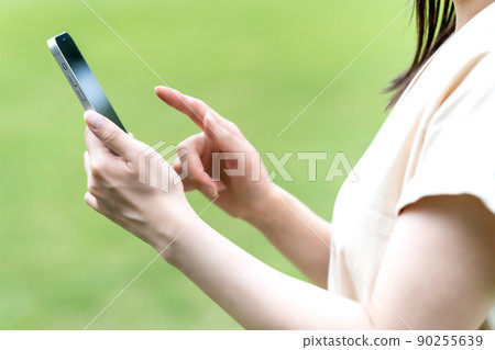 A woman using a smartphone in a green park [Parts cut] 90255639