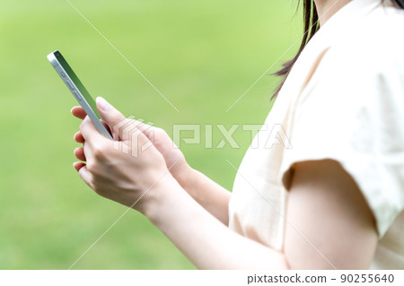 一個在綠色公園裡使用智能手機的女人 [部分切割] 90255640