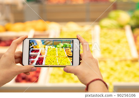 Horizaontal close-up shot of unrecognizable hand holding smartphone with discount application on its screen with fruits on background 90256106