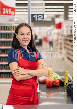 Cheerful woman working in supermarket sitting at cash desk looking at camera smiling Cheerful woman working in supermarket sitting at cash desk looking at camera smiling 90256421