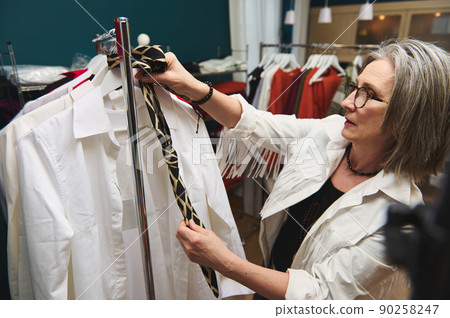 Elderly white-haired elegant and modern Caucasian female fashion designer, couturier stylist, tailor in a tailoring atelier with women's clothing exclusive collection showroom Elderly white-haired elegant and modern Caucasian female fashion designer, couturier stylist, tailor in a tailoring atelier with women's clothing exclusive collection showroom 90258247