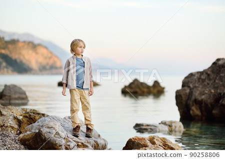 Cute schoolchild hiking by rocks near sea, having fun and exploring nature. 90258806