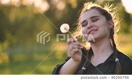 A young girl gently looks at the dandelion flower. 90260798