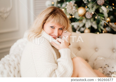 attractive woman blonde in white sweater in room decorated for New Year.  90260877