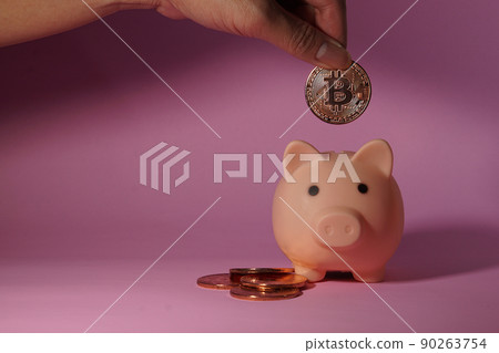 Hand of man drops metal bitcoin coin into piggy bank. Business and Finance. Hand of man drops metal bitcoin coin into piggy bank. Business and Finance. 90263754