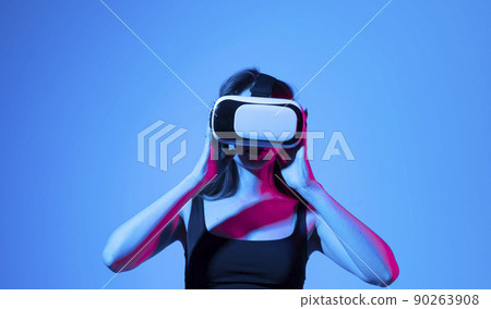 Concept of modern gadgets and technologies. Future technology concept. Portrait of young woman in VR-glasses in neon light on blue background. Virtual reality gaming. 90263908