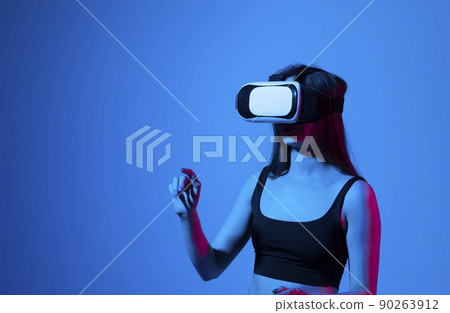Portrait of young woman playing in VR-glasses in neon light on blue background. Concept modern gadgets and technologies. Future technology concept. Virtual reality gaming. 90263912