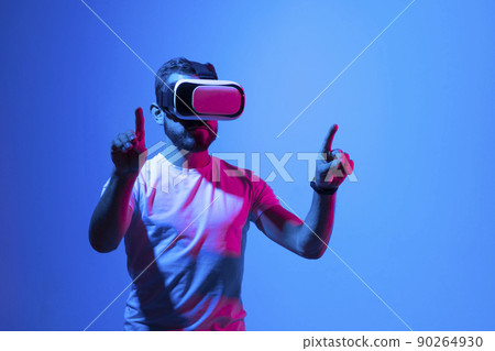 Bearded man playing VR video game in metaverse with virtual reality goggles and trying to touch something. Future technology concept. 90264930