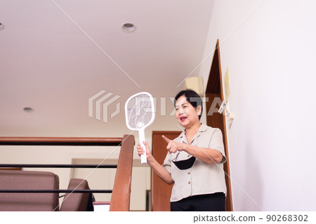 Elderly woman using mosquito swatter at home,Senior women with mosquito electric net racket Elderly woman using mosquito swatter at home,Senior women with mosquito electric net racket 90268302