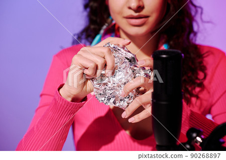 Selective focus of young woman creating content for ASMR blog squeezing foil in front of microphone 90268897