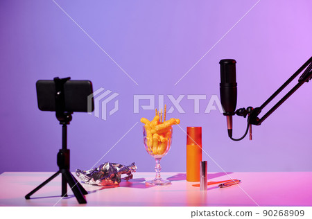 No people still life shot of microphone, smartphone on tripod, glass with crunchy snacks, foil and cosmetic products on table prepared for ASMR No people still life shot of microphone, smartphone on tripod, glass with crunchy snacks, foil and cosmetic products on table prepared for ASMR 90268909