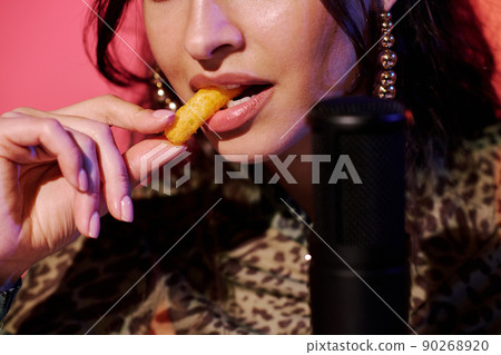 Modern young female influencer sitting in studio in pink neon light recording crunchy corn puff snacks eating sounds for ASMR vlog Modern young female influencer sitting in studio in pink neon light recording crunchy corn puff snacks eating sounds for ASMR vlog 90268920