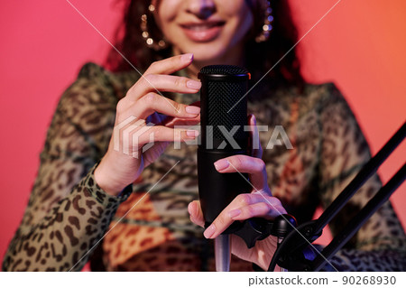 Selective focus of young female blogger sitting in studio in pink and yellow neon light recording sounds for ASMR vlog scratching microphone 90268930