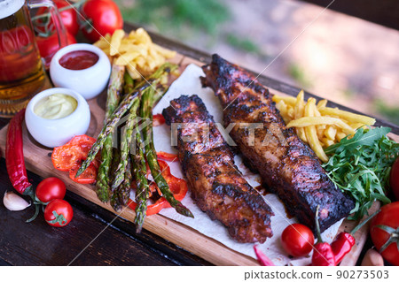Barbecue pork ribs on wooden serving board on picnic table outdoors Barbecue pork ribs on wooden serving board on picnic table outdoors 90273503