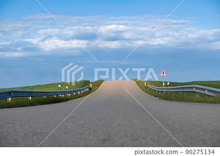 Asphalt road leading through lush green fields 90275134