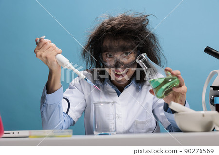Grinning creepy lunatic silly looking mad scientist with dropper and beaker mixing experimental liquid chemical substances. Crazy chemist with dreadful face expression doing laboratory work. Grinning creepy lunatic silly looking mad scientist with dropper and beaker mixing experimental liquid chemical substances. Crazy chemist with dreadful face expression doing laboratory work. 90276569