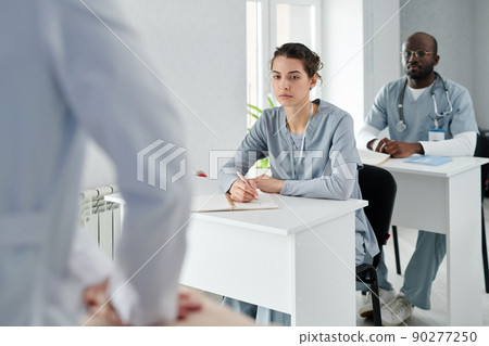 Medical students in uniform sitting at desks learning how to provide first aid during training Medical students in uniform sitting at desks learning how to provide first aid during training 90277250