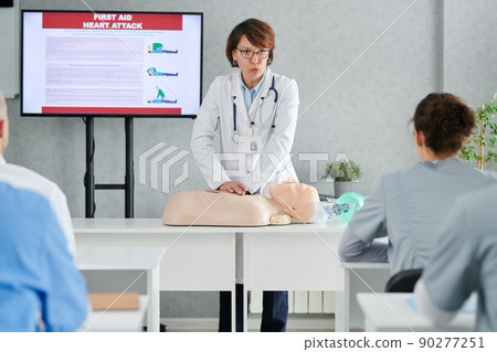 Medical specialist demonstrating on mannequin how to providing first aid to students at training 90277251