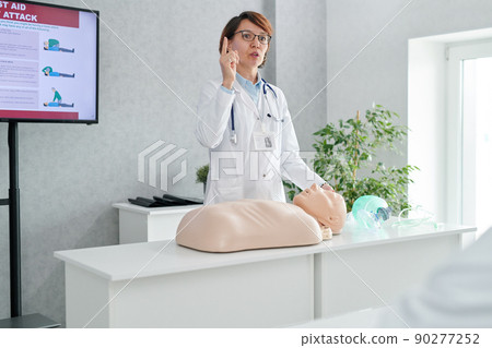 Mature female doctor talking about the rules of first aid using mannequin during medical training Mature female doctor talking about the rules of first aid using mannequin during medical training 90277252