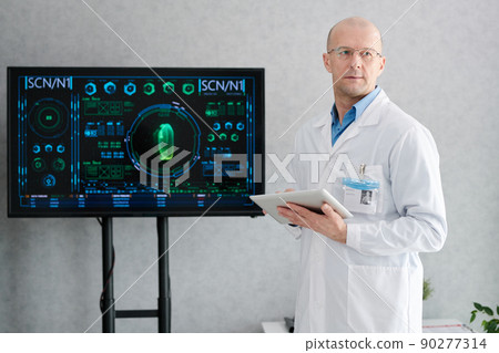 Serious mature doctor in white coat standing near the big display and using tablet pc during conference Serious mature doctor in white coat standing near the big display and using tablet pc during conference 90277314