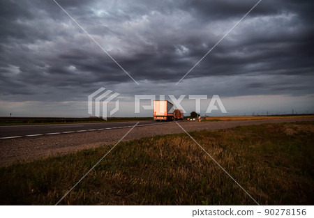 A column of trucks with trailers carry cargo in the evening against a cloudy sky with clouds. Direct FTL transportation model. Copy space for text, expedited shipping 90278156