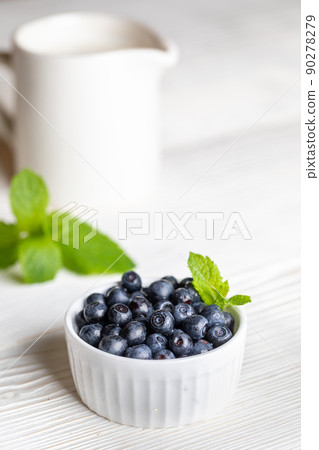 Bowl with forest blueberries and white milk jug with milk on white wooden background. Blueberry - natural superfood. Healthy food. Vertical orientation. Selective focus. Bowl with forest blueberries and white milk jug with milk on white wooden background. Blueberry - natural superfood. Healthy food. Vertical orientation. Selective focus. 90278279