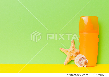 Beach accessories. Moisturiser sunscreen suntan lotion bottle for UVB skincare protection in summer with seashells on colored background. Mock up with copy space 90279072