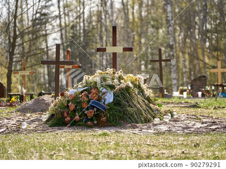 New grave with wooden cross and several funeral wreaths. Another graves with crosses behind it. Forest at the background. New grave with wooden cross and several funeral wreaths. Another graves with crosses behind it. Forest at the background. 90279291