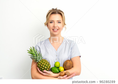 Portrait of a young caucasian smiling female nutritionist with different fruits in her hands over white background Portrait of a young caucasian smiling female nutritionist with different fruits in her hands over white background 90280289