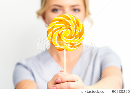 Waxing, depilation concept. The beautician is wearing a medical coat holding a sugar lollipop on white background Waxing, depilation concept. The beautician is wearing a medical coat holding a sugar lollipop on white background 90280290