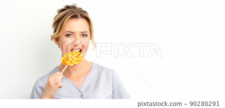 Portrait of a beautiful young caucasian beautician wearing a medical shirt bites a lollipop on a white background Portrait of a beautiful young caucasian beautician wearing a medical shirt bites a lollipop on a white background 90280291