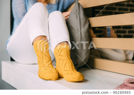 Comforting cozy woman in knitted woolen winter yellow socks, white trousers and blue warm sweater resting sitting on a bench at cafe in winter time. Lazy day in knitted socks at cafe. Cozy time Comforting cozy woman in knitted woolen winter yellow socks, white trousers and blue warm sweater resting sitting on a bench at cafe in winter time. Lazy day in knitted socks at cafe. Cozy time 90280993