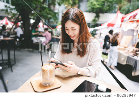Young adult asian woman using smart phone at outdoor cafe on weekend Young adult asian woman using smart phone at outdoor cafe on weekend 90283947