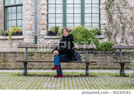 Fashionable white woman sitting on a bench with an historic building in the background 90284581