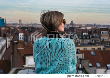 Portrait of an attractive thirty year old white woman with sunglasses posing on her rooftop with the Brussels skyline during sunset in the background 90284582
