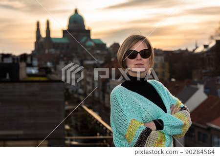 Portrait of an attractive thirty year old white woman with sunglasses posing on her rooftop with the Brussels skyline during sunset in the background 90284584