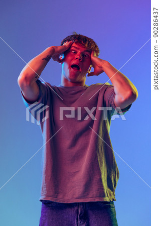 Young red-headed man, student grimacing isolated over blue studio background in neon light. Concept of youth, fashion, emotions, facial expression Young red-headed man, student grimacing isolated over blue studio background in neon light. Concept of youth, fashion, emotions, facial expression 90286437
