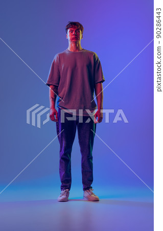 Grimace. Young red-headed man, student isolated over blue studio background in neon light. Concept of youth, fashion, emotions, facial expression Grimace. Young red-headed man, student isolated over blue studio background in neon light. Concept of youth, fashion, emotions, facial expression 90286443