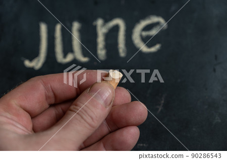 Adult male holding a piece of yellow chalk in his hand. Handwritten word JUNE on black chalkboard. Selective focus. Adult male holding a piece of yellow chalk in his hand. Handwritten word JUNE on black chalkboard. Selective focus. 90286543