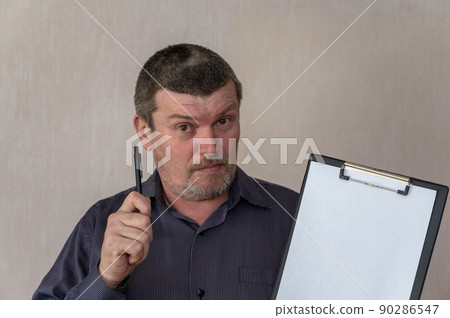 Portrait of an adult male holding a clipboard and pen. Man with short haircut and graying hair. White blank piece of paper clutched in clipboard. Looking into the camera. Indoors. Portrait of an adult male holding a clipboard and pen. Man with short haircut and graying hair. White blank piece of paper clutched in clipboard. Looking into the camera. Indoors. 90286547