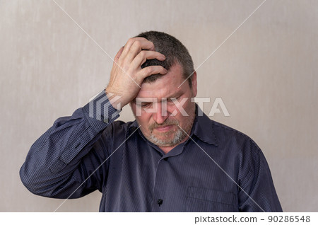 Portrait of an adult annoyed man looking down. The man in the blue striped shirt put his hand on his head. Short brown hair with gray. Portrait of an adult annoyed man looking down. The man in the blue striped shirt put his hand on his head. Short brown hair with gray. 90286548