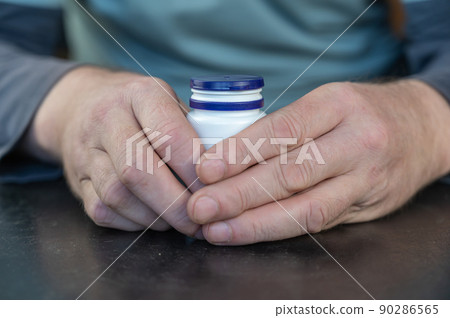An adult man holds a white vial in his hands. An adult man holds a white vial in his hands. 90286565