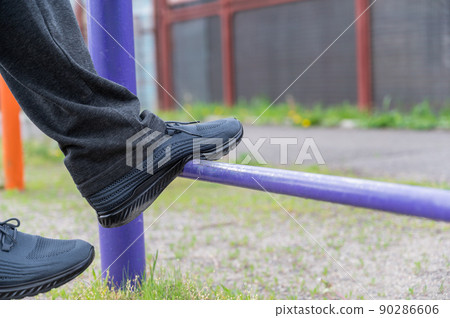 The lower section of a mature man exercising on an outdoor sports field. Legs of a man straining on athletic trainers. Gymnastic exercises. The lower section of a mature man exercising on an outdoor sports field. Legs of a man straining on athletic trainers. Gymnastic exercises. 90286606