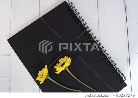 Black note book flat lay with sunflowers on wooden desk. Directly above. Black note book flat lay with sunflowers on wooden desk. Directly above. 90287279