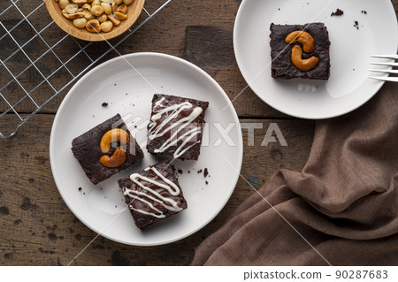 Chocolate Brownie topping with cashew nut on white plate.Delicious taste bitter sweet, chewy and fudge.Top view Chocolate Brownie topping with cashew nut on white plate.Delicious taste bitter sweet, chewy and fudge.Top view 90287683