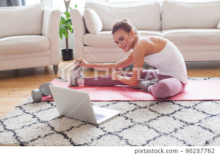 Young fit cute smiling woman doing fitness exercises on pink mat indoors at home interior 90287762