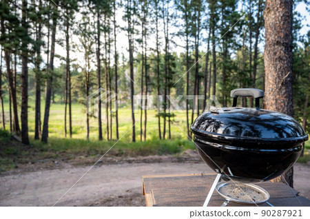 Focus on a portable charcoal grill at a campsite overlooking a green forest 90287921