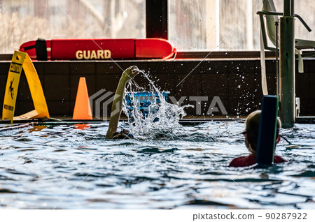 Youth swimming lesson in indoor pool. Swimmers backlit and silhouette with light reflecting off of water surface. Youth swimming lesson in indoor pool. Swimmers backlit and silhouette with light reflecting off of water surface. 90287922